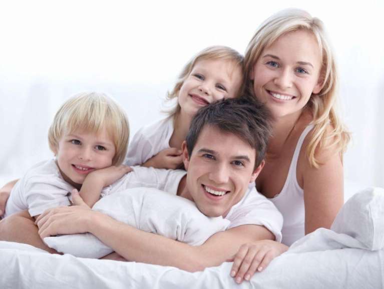 Family smiling on bed | Reservoir Dentist